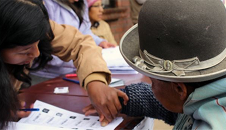 Mujer indígena participa en un proceso electoral con la asistencia de un funcionario de casilla.   