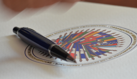 una pluma sobre un documento con el sello de la OEA