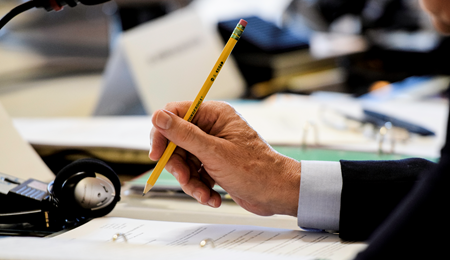 una mano de hombre sujetando un lápiz sobre un papel en una reunión