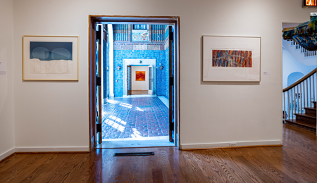 An open door to a hallway with blue walls; a painting hanging on each side